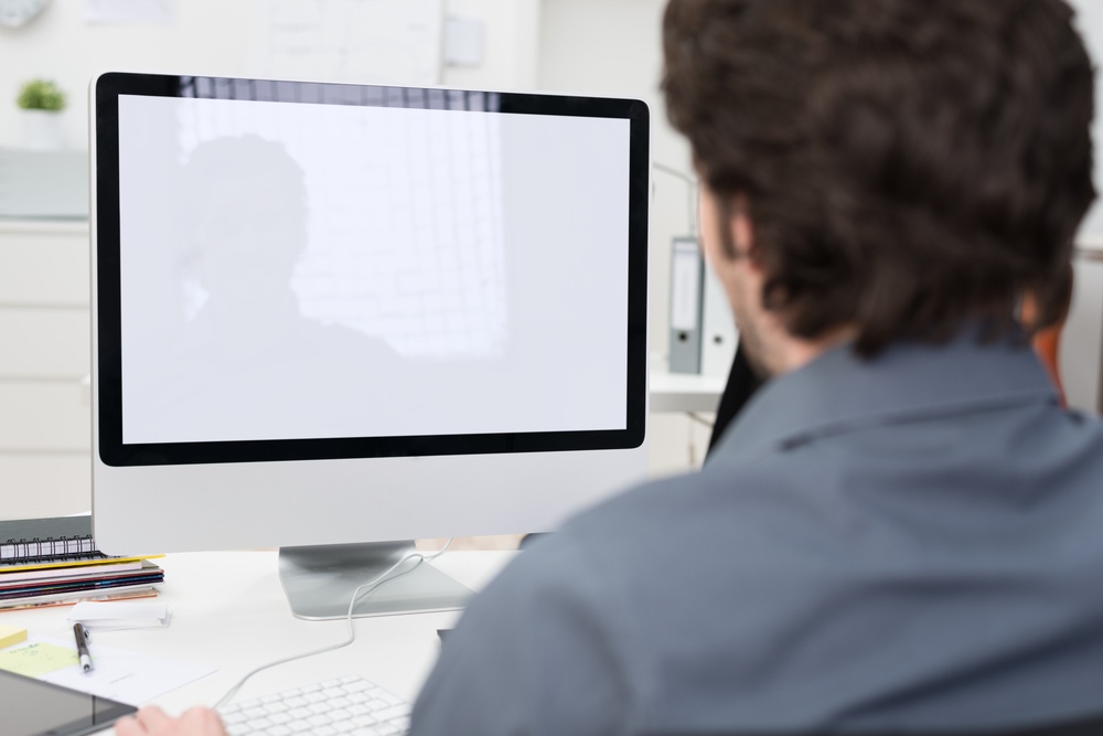 Businessman using a desktop computer with a view over his shoulder from behind of the blank screen of the monitor