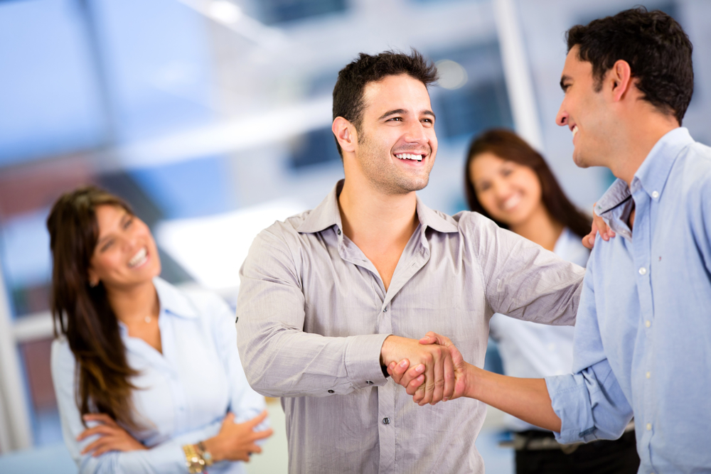 two men shaking hands with two women in background. Know, Like and Trust