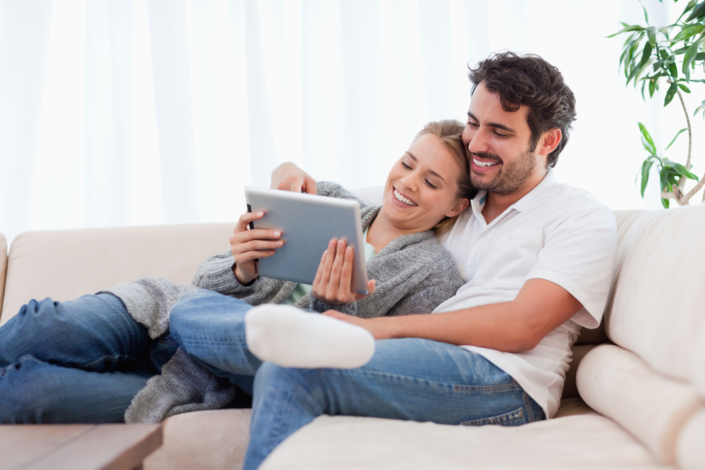 Happy couple using a tablet computer in their living room - engaging with something on screen