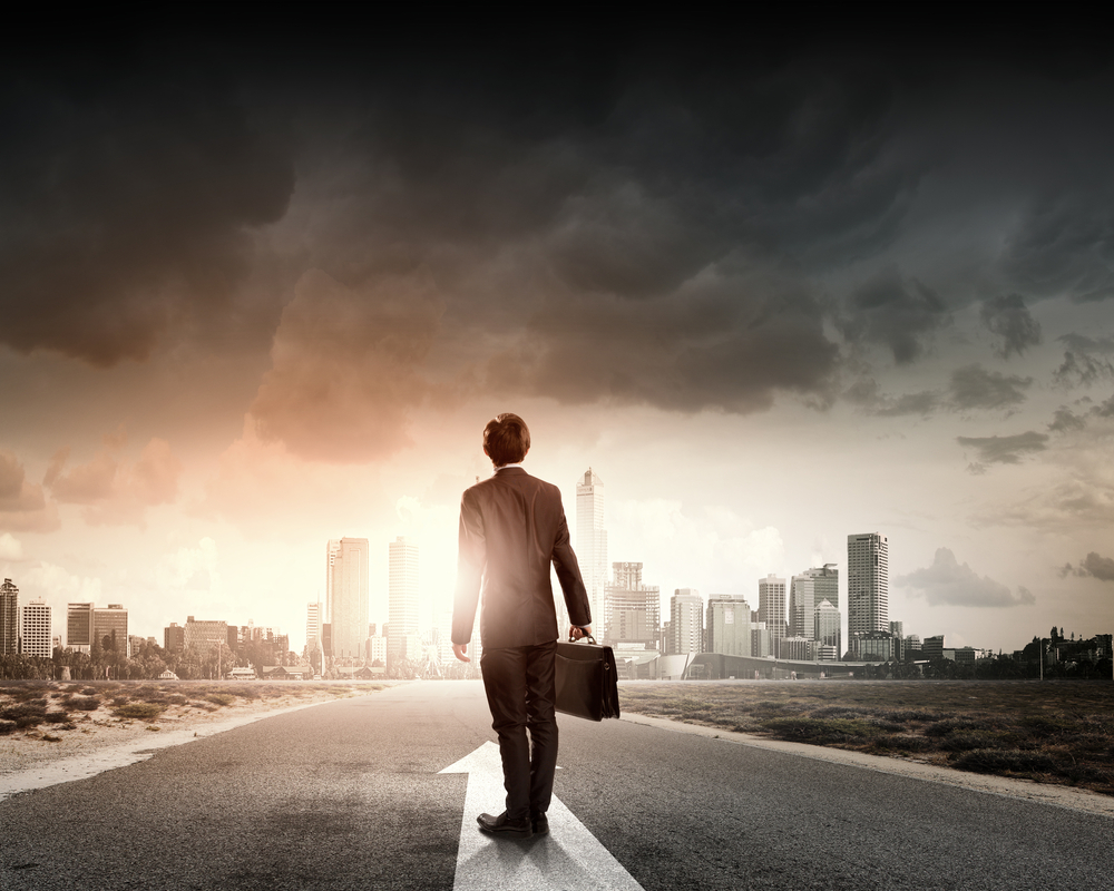 businessman holding briefcase standing on road looking ahead